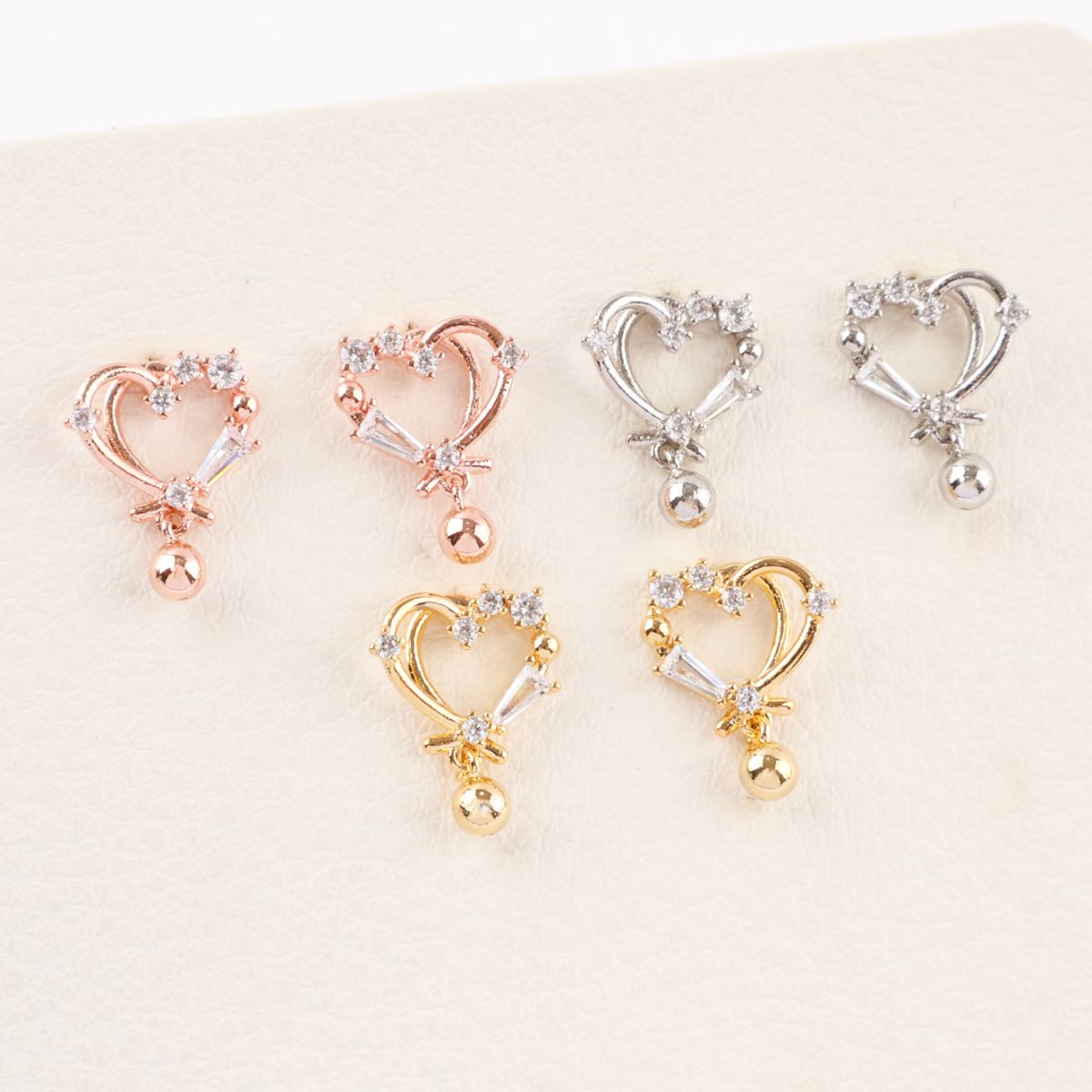 Six heart earrings in three finishes displayed on cream background, rose gold silver gold plated options with cubic zirconia, romantic drop design with ball charms, 925 posts, Korean jewelry collection