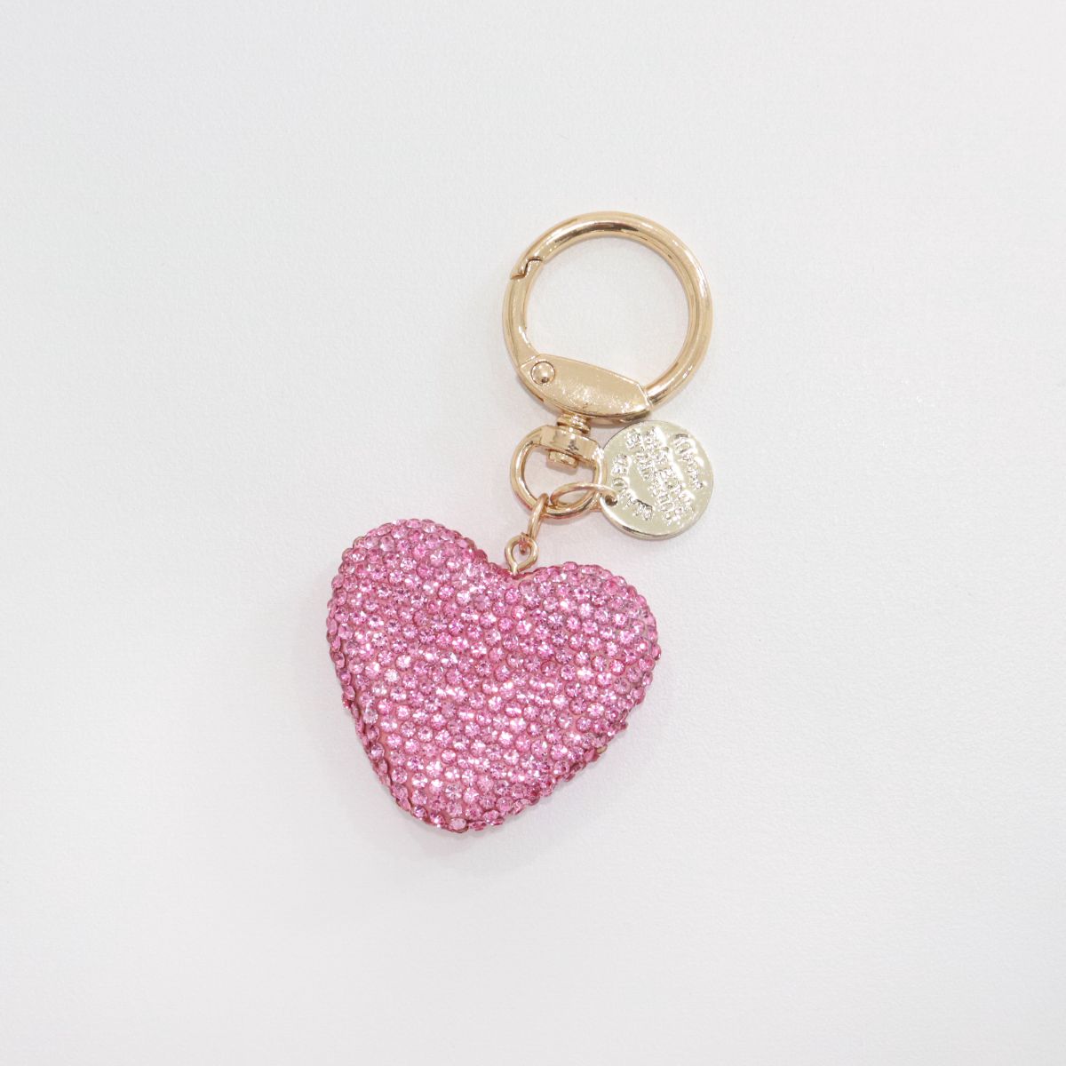A single pink rhinestone heart keychain laid flat on a white surface.
Gold keyring and medallion attached to the top.