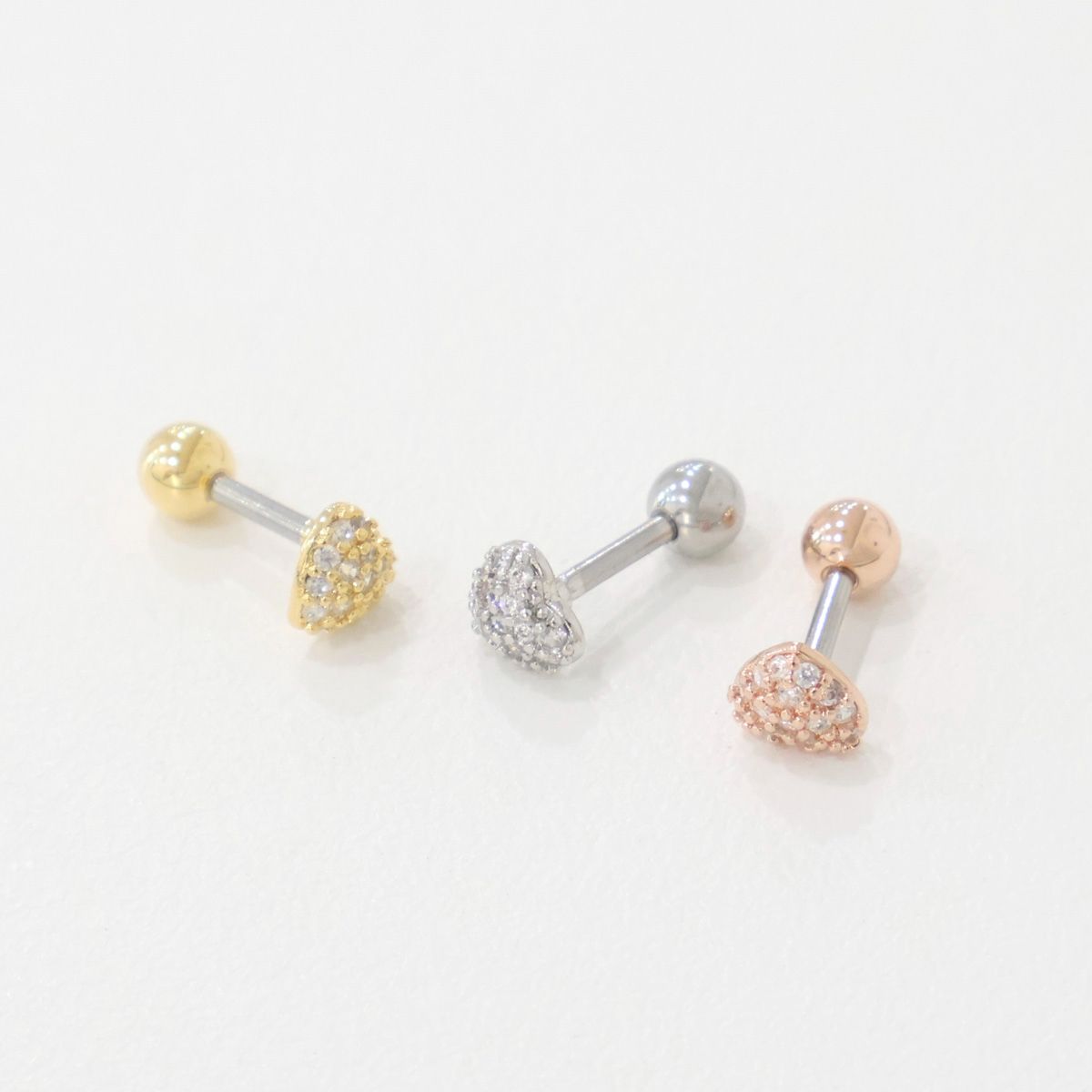Gold, silver, and rose gold pavé heart barbell earrings photographed from the side to show thickness.