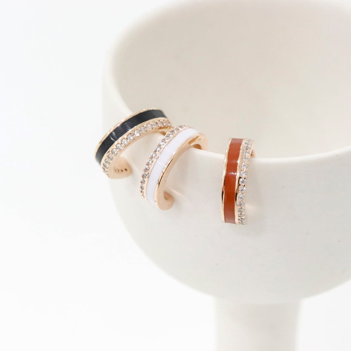 Black, white, and brown enamel ear cuffs with crystal trim, styled on minimal ceramic cup
