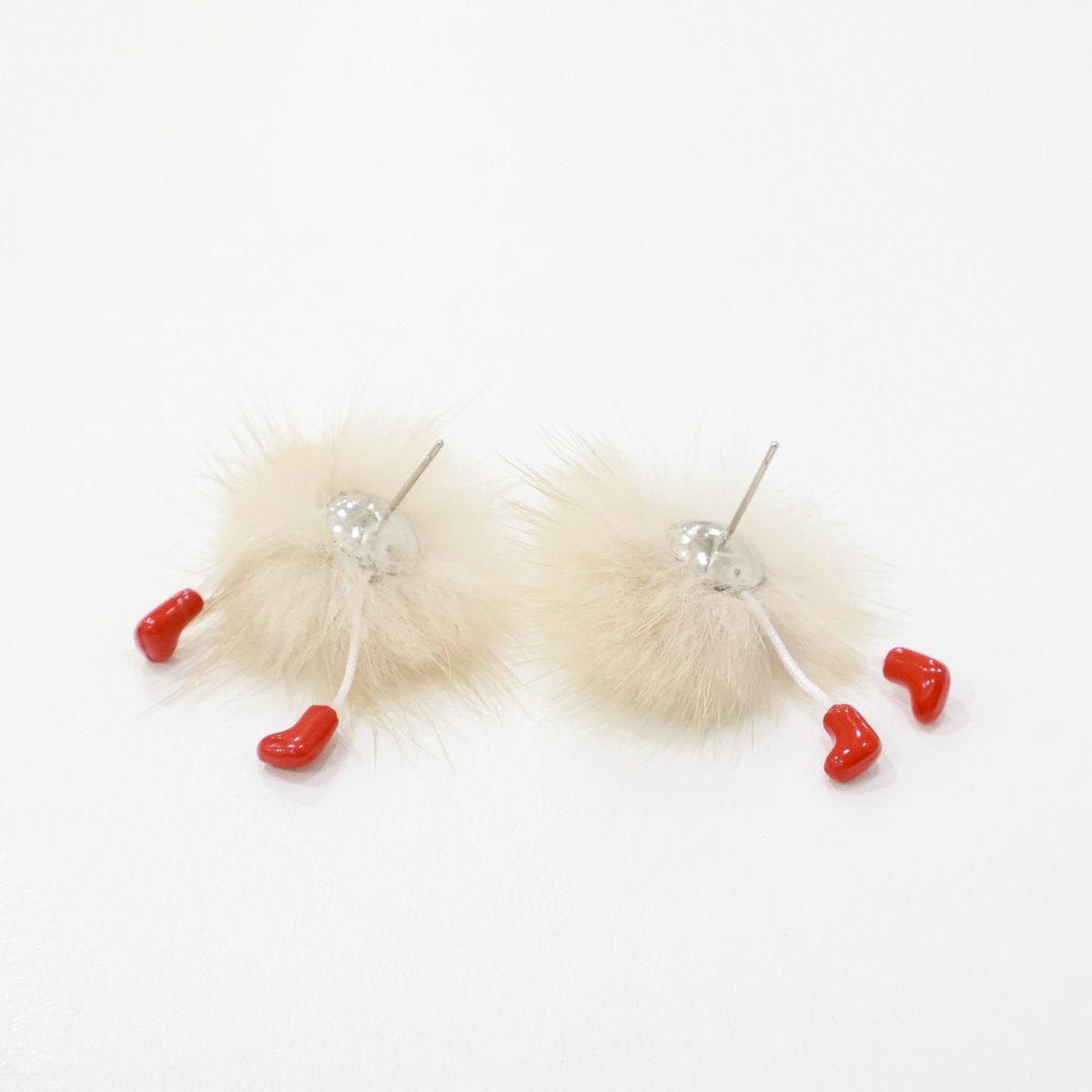 Back view of a fluffy beige earring showing the silver post and dangling red feet.