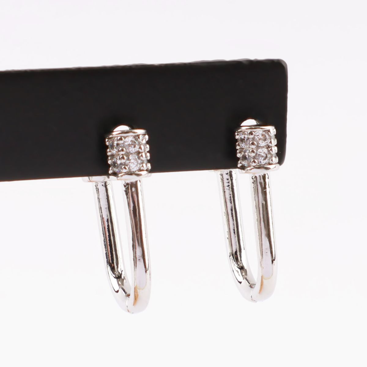 Silver pavé hoop earrings displayed on a black holder, showcasing the crystal cylinder clasp in detail.