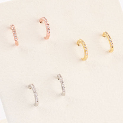 Six pairs of cubic zirconia half hoop earrings neatly arranged on a cream-colored velvet display, in silver, gold, and rose gold.