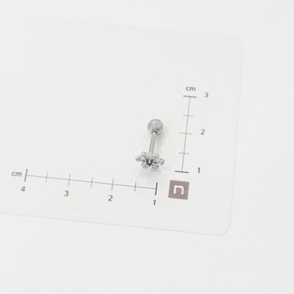 Snowflake barbell piercing with blue center stone placed on a measurement chart, showing approx. 1.3cm width.