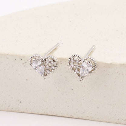 White gold heart stud earrings featuring pear-cut cubic stones, standing upright against a curved stone-textured backdrop.