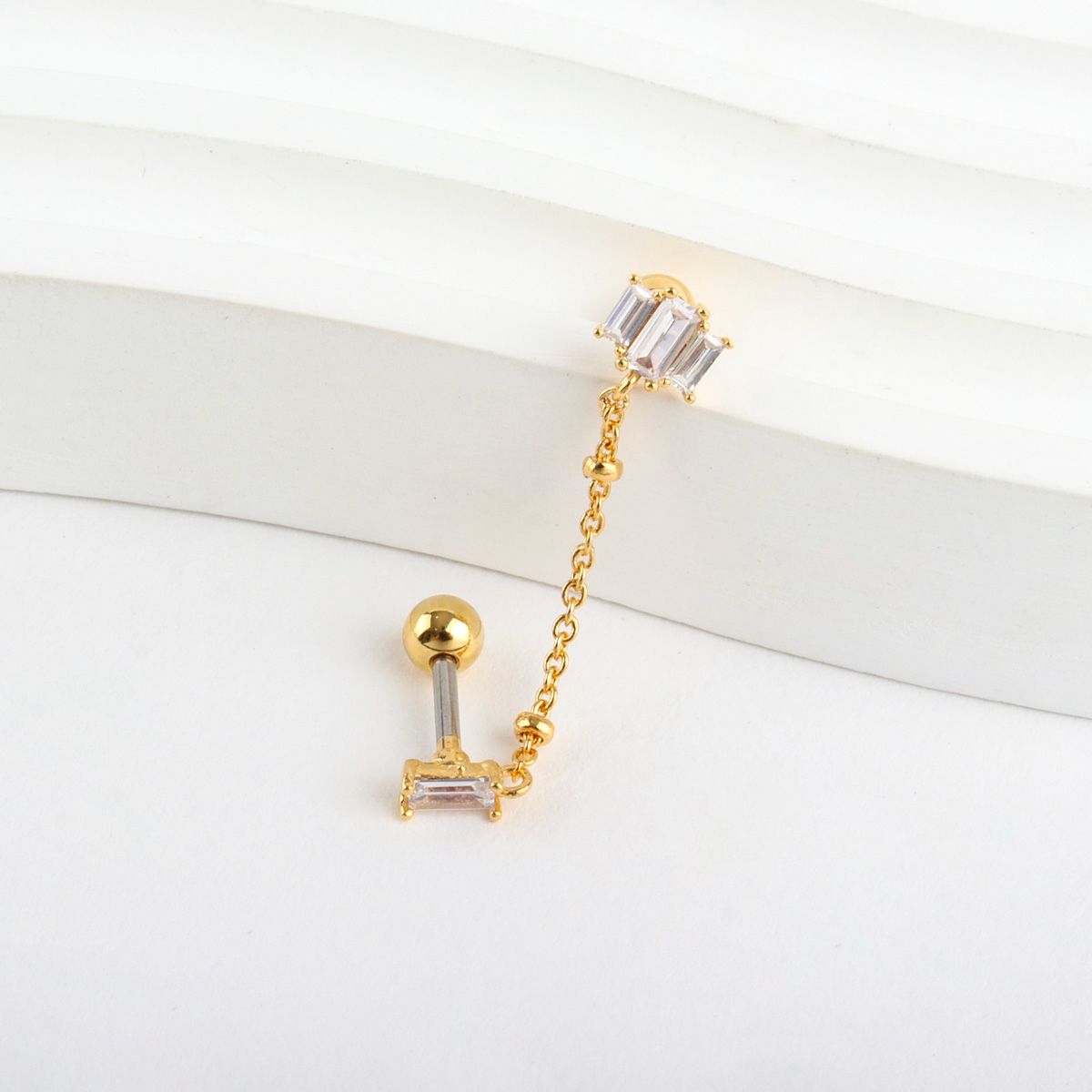 Close-up product detail showing surgical steel post and brass chain with crystal