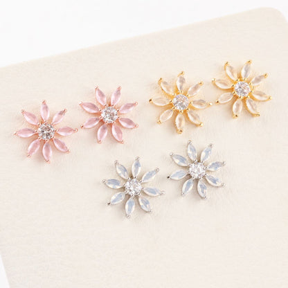 Six flower-shaped earrings in gold, pink, and silver tones displayed on a cream-colored textured surface.