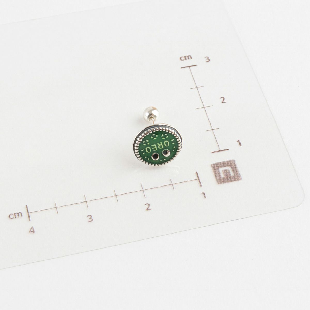 Size measurement of green Oreo piercing with 925 silver post and ruler on white background