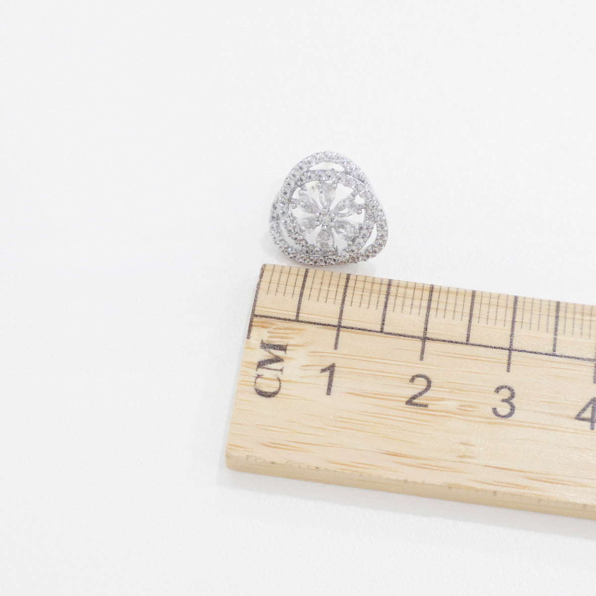Silver heart CZ stud earring with wooden ruler showing size approximately 10mm, flower motif detail, 925 sterling silver posts Korean made