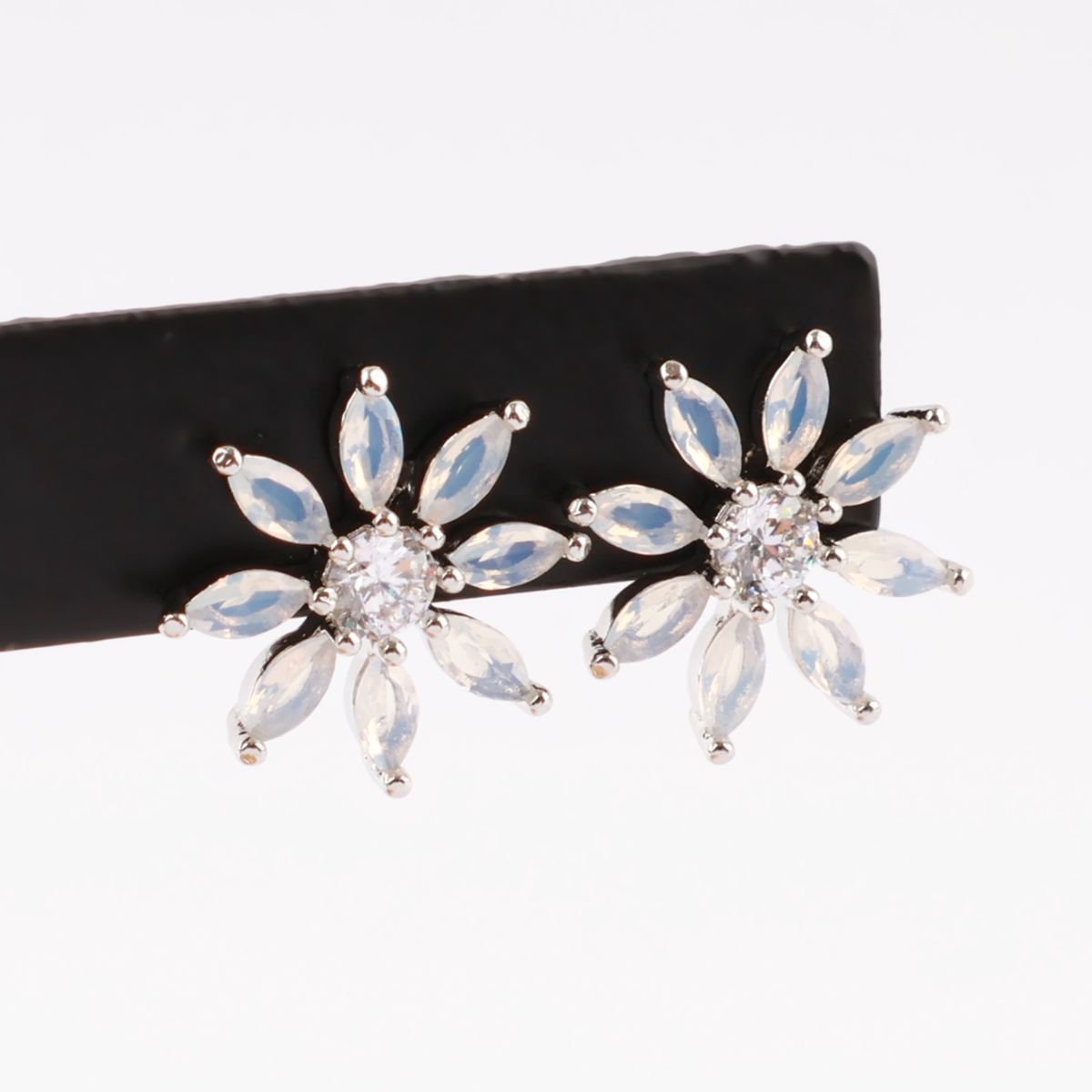 Pair of silver-tone floral earrings with translucent marquise-cut stones displayed on a black bar.
