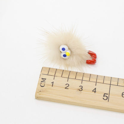 Fluffy beige character earring placed beside a ruler for size reference
