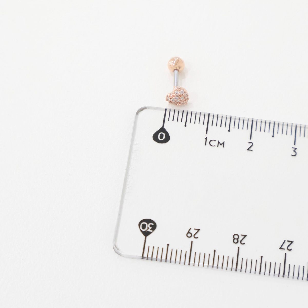 Rose gold pavé heart barbell earring next to a clear ruler showing size in centimeters.