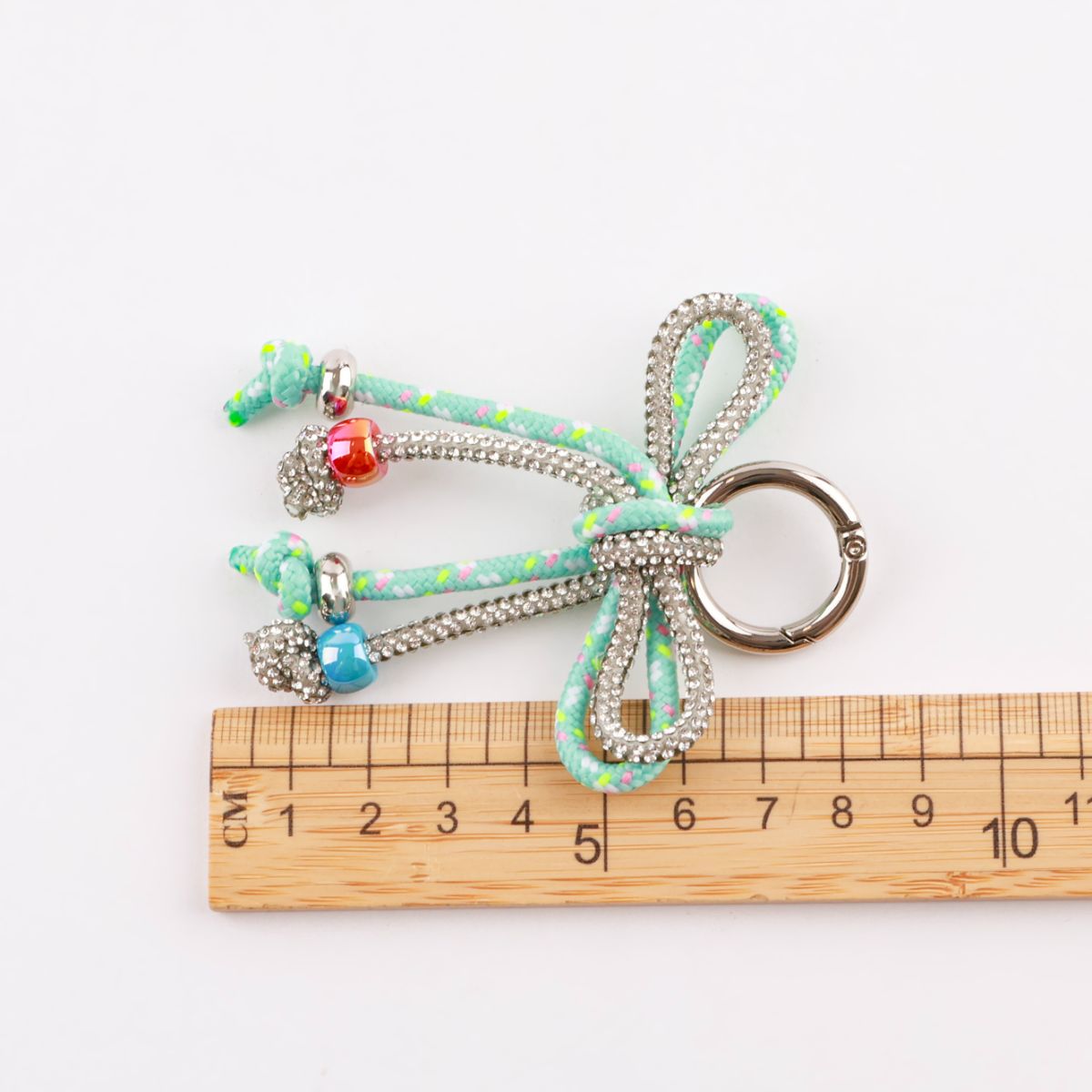 Mint dotted rope bow bag charm next to ruler showing 7-8cm width size comparison