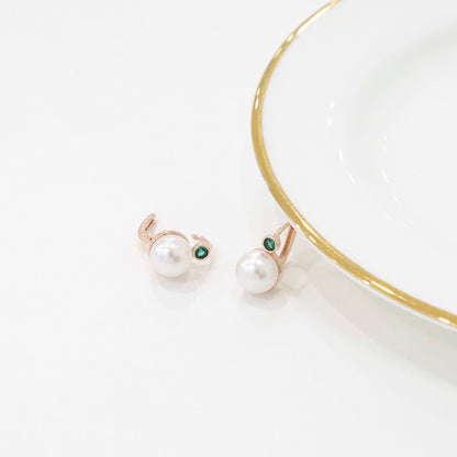 A pair of green-stone pearl drop earrings placed beside a white and gold-rimmed ceramic plate.