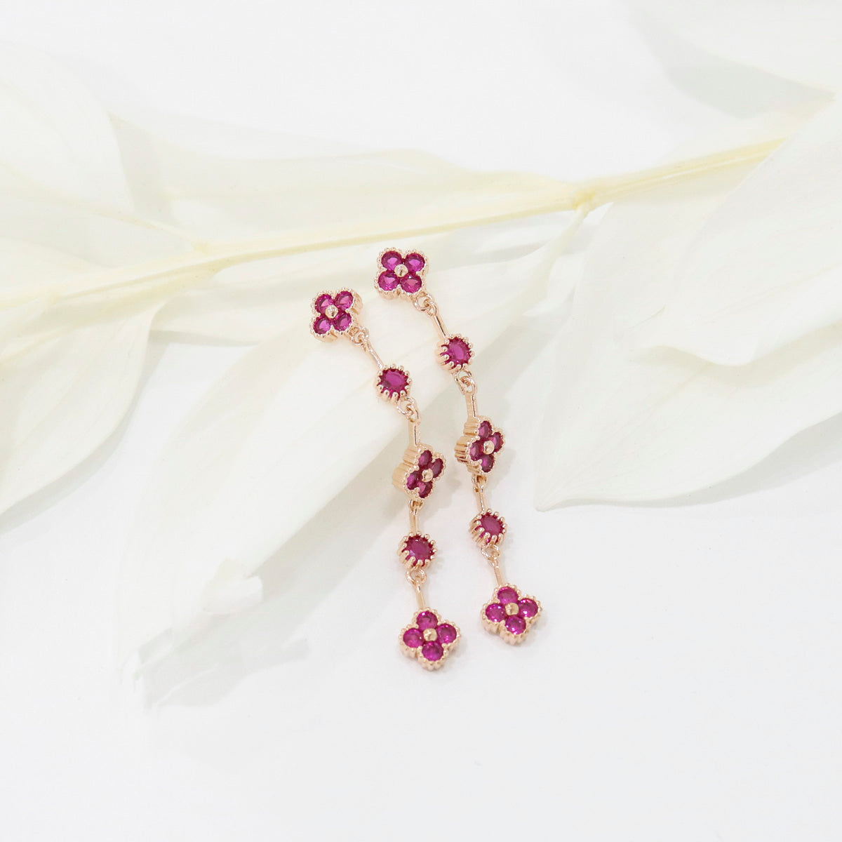 Close-up of ruby red clover drop earrings showing milgrain setting and cubic zirconia sparkle