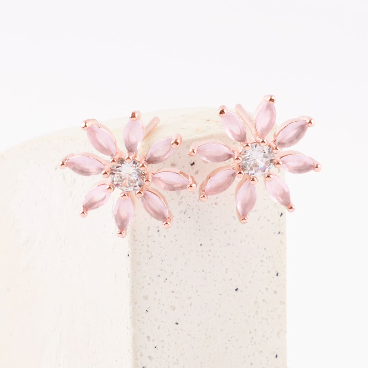 Pink-tone flower-shaped stud earrings with marquise-cut stones and central cubic zirconia, styled on a stone pedestal