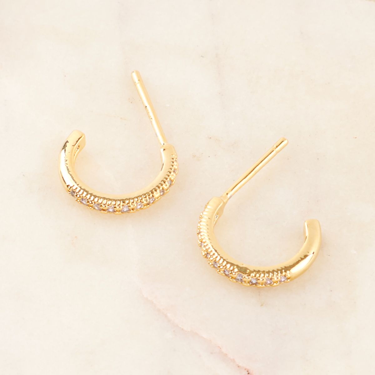 Gold mini hoop earrings with cubic zirconia lined on the front, placed on a warm marble surface.

Image 6