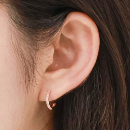 Rose gold mini hoop earring worn on a woman's earlobe, shown from the side.