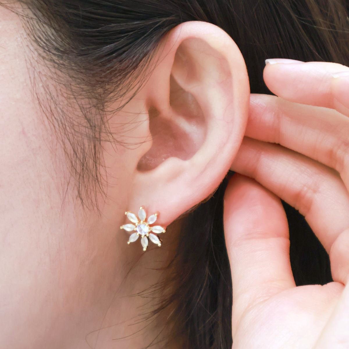 Close-up of a gold floral stud earring with white stones worn on the left ear.