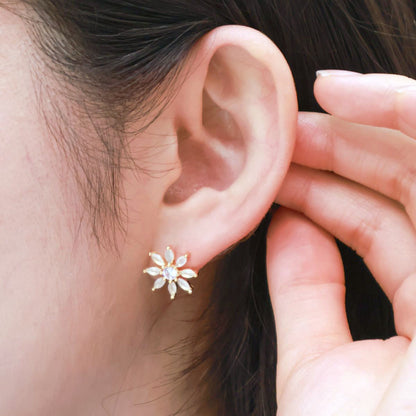 Close-up of a gold floral stud earring with white stones worn on the left ear.