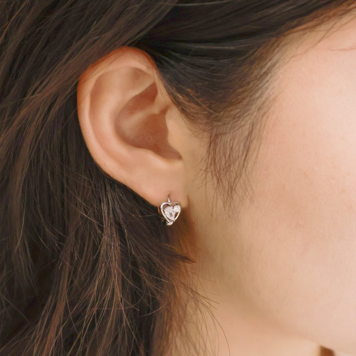 Woman wearing the silver heart huggie earring on the left earlobe; simple and elegant styling.