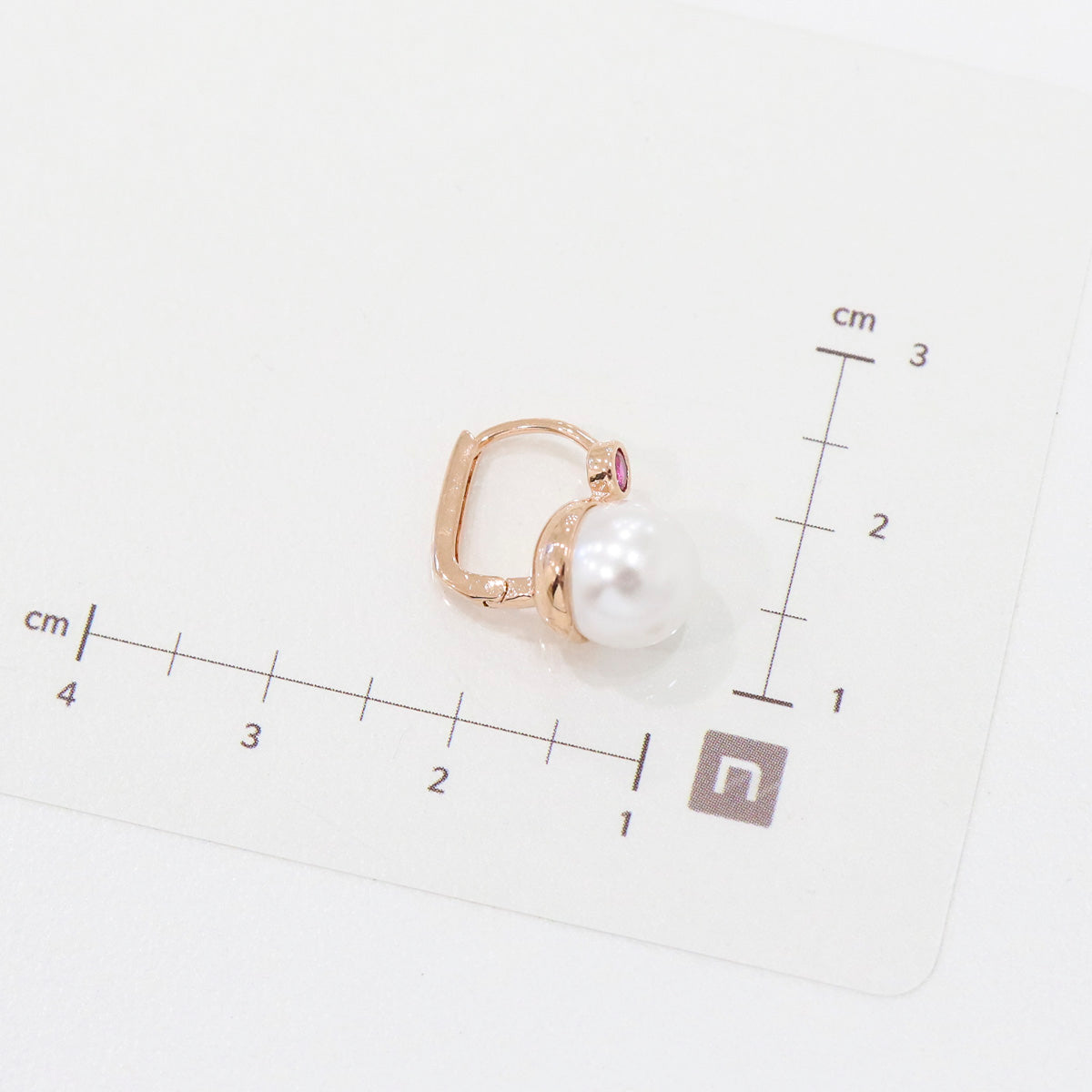 One pink-stone pearl drop earring laid on a measurement grid in centimeters for size reference.
