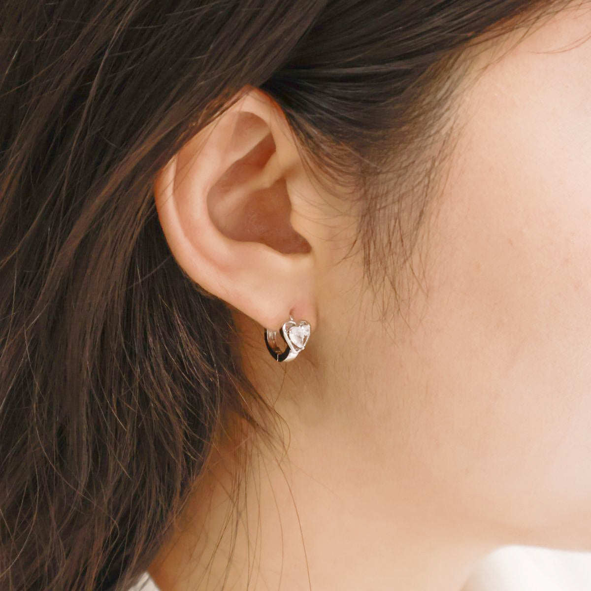 Side view of silver mini heart hoop earring worn on the right earlobe; lightweight and snug fit.