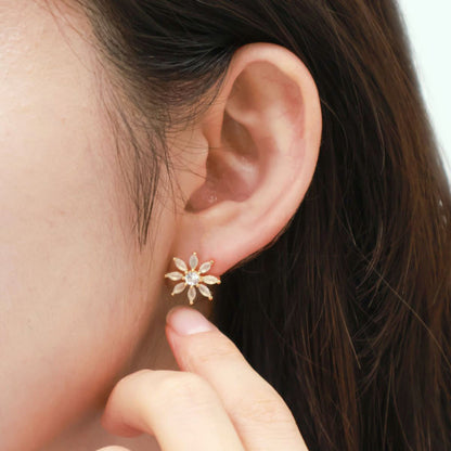 Side view of a gold floral stud earring worn on the left ear, with hand touching the earlobe.