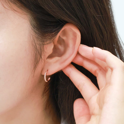 Side angle of a woman adjusting her rose gold hoop earring with her hand, highlighting fit and shine.