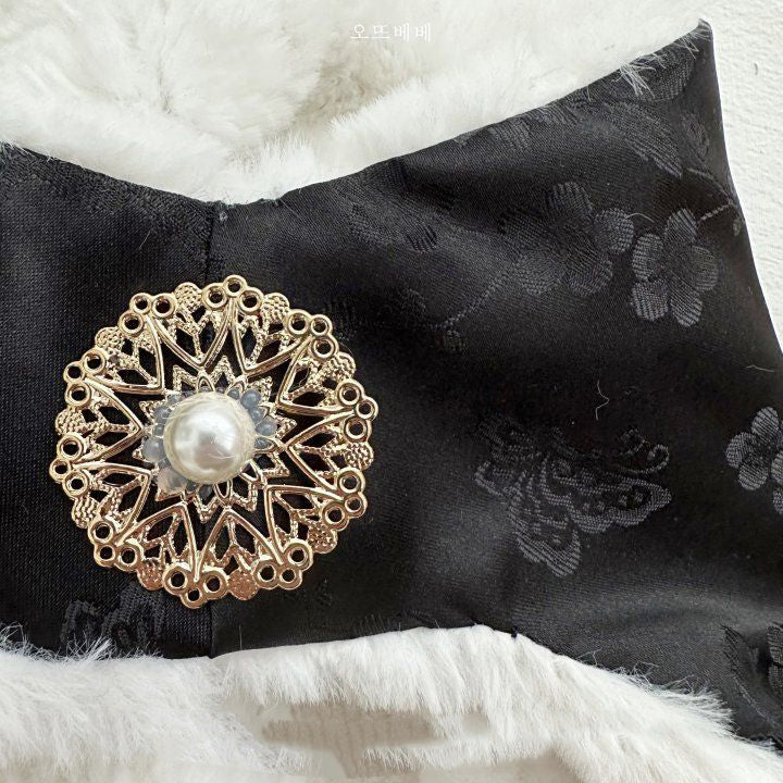 Macro view of a gold brooch with pearl center, pinned on the black satin collar with subtle floral jacquard pattern.