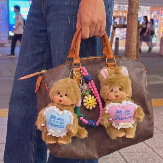 Urban kitsch bag charm look — Monchhichi blue heart classic on Louis Vuitton Damier tote, K-style bag decoration inspo with purple smile bead strap.