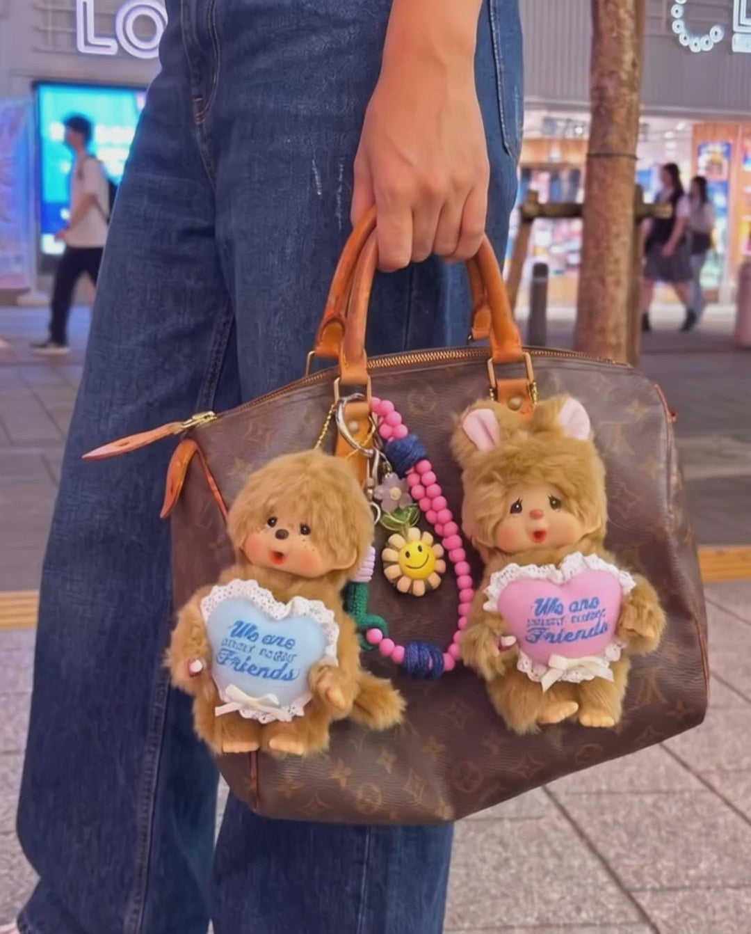 Urban kitsch bag charm look — Monchhichi blue heart classic on Louis Vuitton Damier tote, K-style bag decoration inspo with purple smile bead strap.