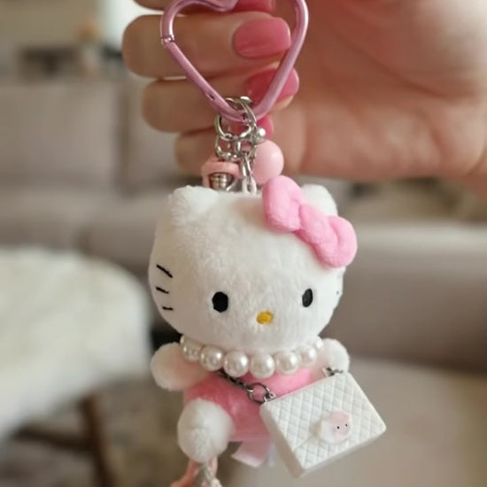 Animated view of Hello Kitty plush keychain held by hand showing heart carabiner and crystal rope strap details