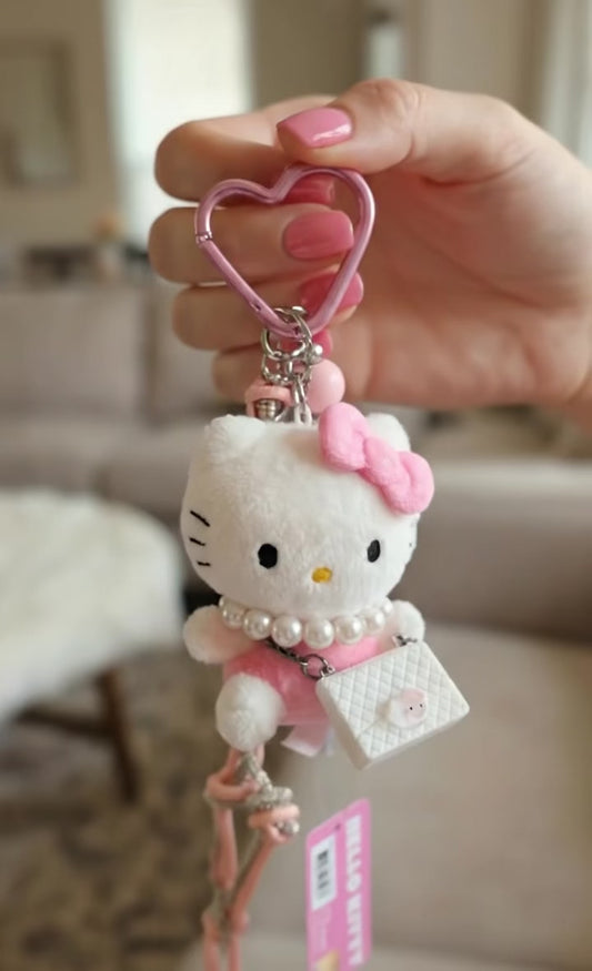 Animated view of Hello Kitty plush keychain held by hand showing heart carabiner and crystal rope strap details