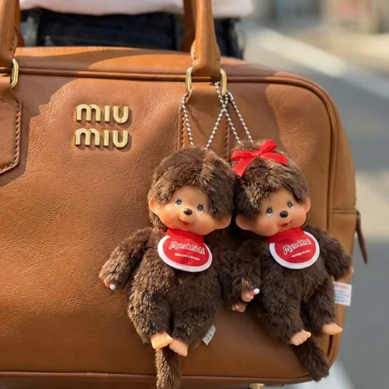 Monchhichi Classic Boy and Ribbon Girl plush keychains paired together on tan Miu Miu bowling bag — couple matching bag charms