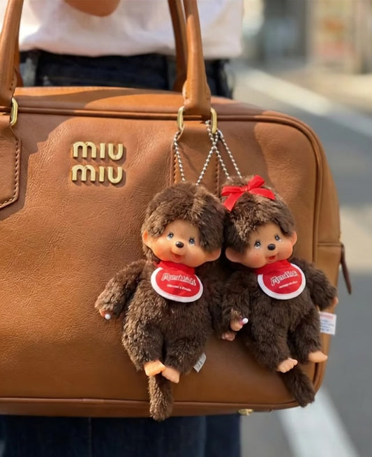 Monchhichi Classic Boy and Ribbon Girl plush keychains paired together on tan Miu Miu bowling bag — couple matching bag charms