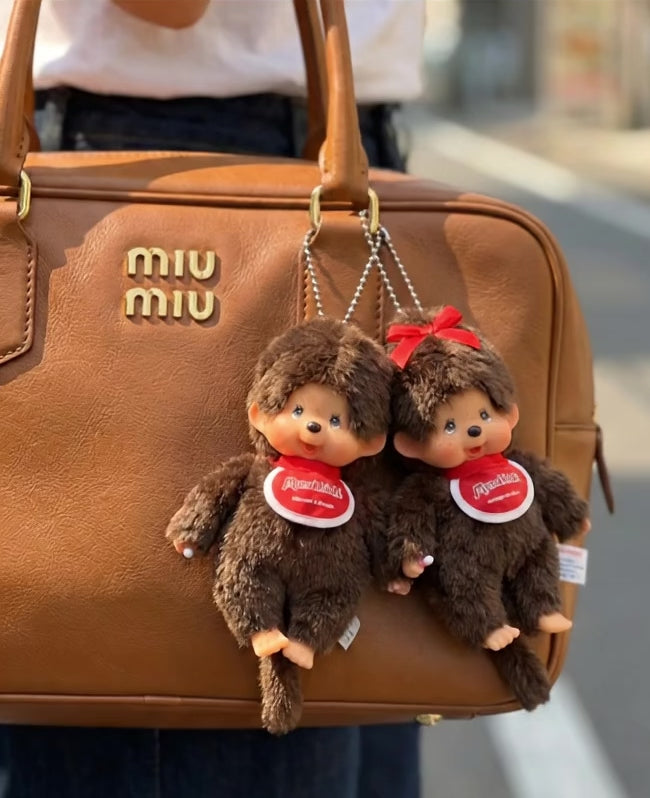 Monchhichi Classic Boy and Ribbon Girl plush keychains paired together on tan Miu Miu bowling bag — couple matching bag charms