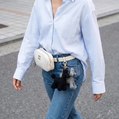 Four handmade needle felted wool poodle keychains in white, brown, grey, and black colors displayed on cream fabric with wooden toys