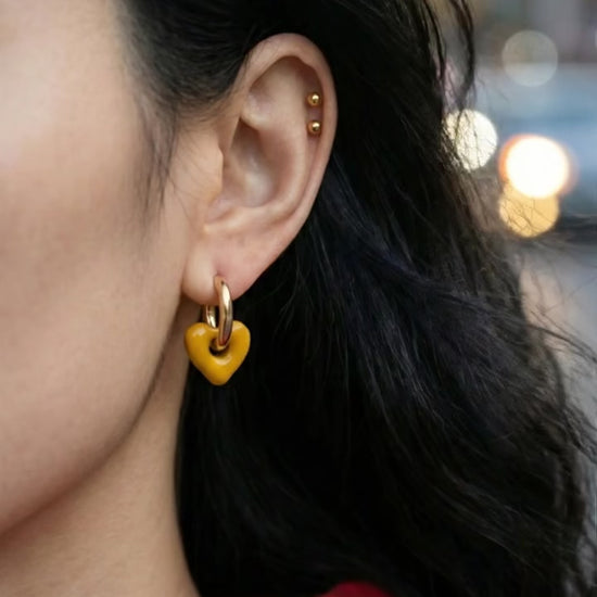 Close-up of woman's ear wearing mustard yellow heart drop earrings with gold cartilage piercings