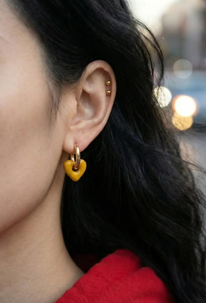 Close-up of woman's ear wearing mustard yellow heart drop earrings with gold cartilage piercings