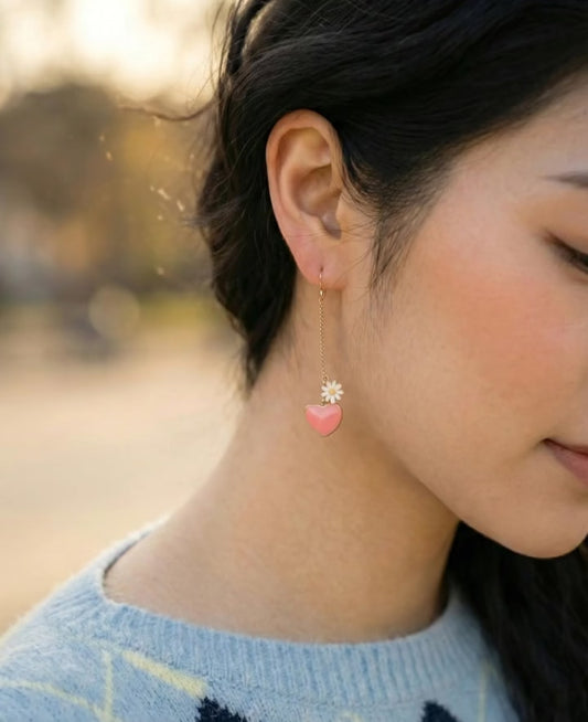 Pink heart and daisy long drop earring worn on ear with delicate gold chain