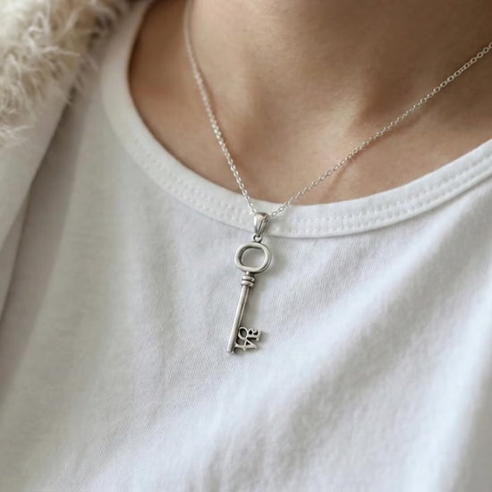  Model wearing the LOVE key necklace over a white t-shirt and fuzzy cream cardigan for a cozy look.