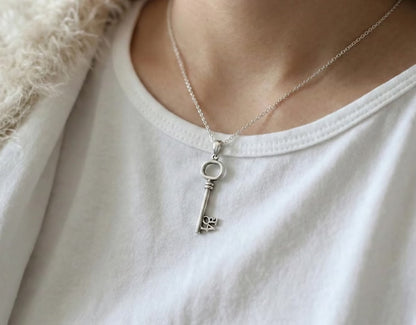  Model wearing the LOVE key necklace over a white t-shirt and fuzzy cream cardigan for a cozy look.