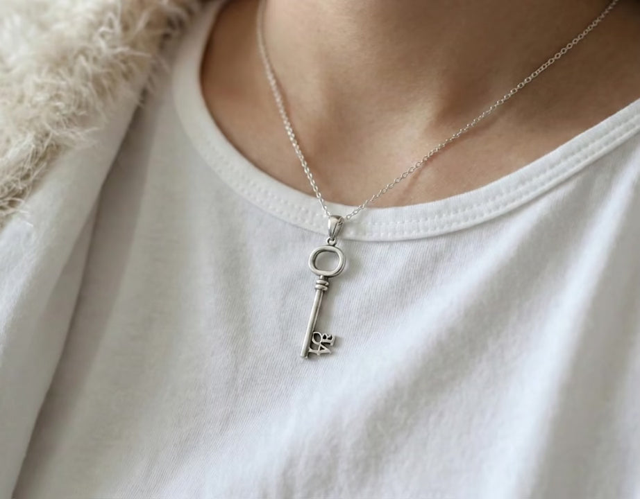  Model wearing the LOVE key necklace over a white t-shirt and fuzzy cream cardigan for a cozy look.