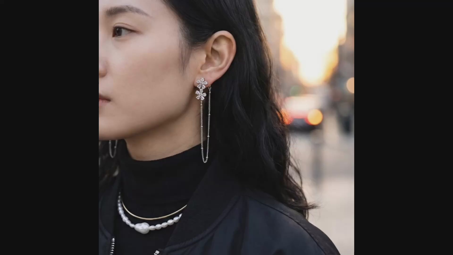 Woman wearing silver floral crystal chain drop earrings with black turtleneck outdoors