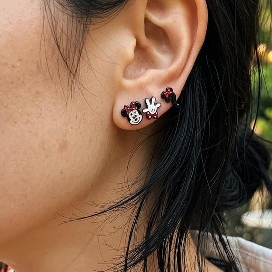 Model wearing mismatched mouse stud earrings in curated ear stack, red striped shirt, layered cut hair.