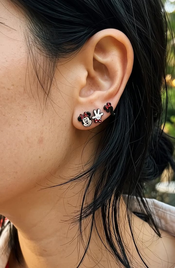 Model wearing mismatched mouse stud earrings in curated ear stack, red striped shirt, layered cut hair.