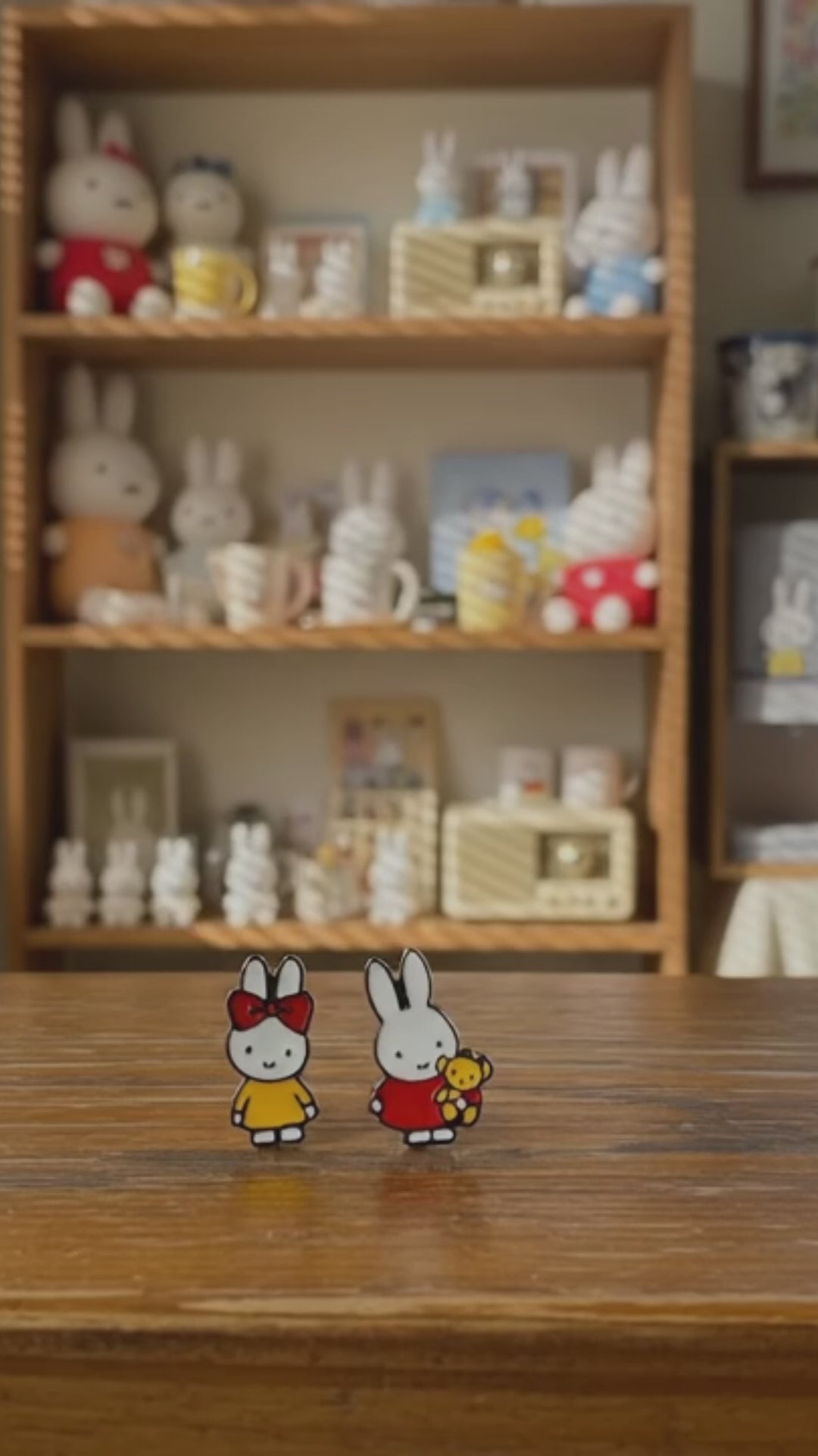 Miffy character earring set displayed on white card with rainy window background, featuring red and yellow enamel studs with 925 sterling silver hypoallergenic posts, Korean handmade kawaii jewelry, cozy lifestyle aesthetic with soft blue pillow and Miffy plush toys